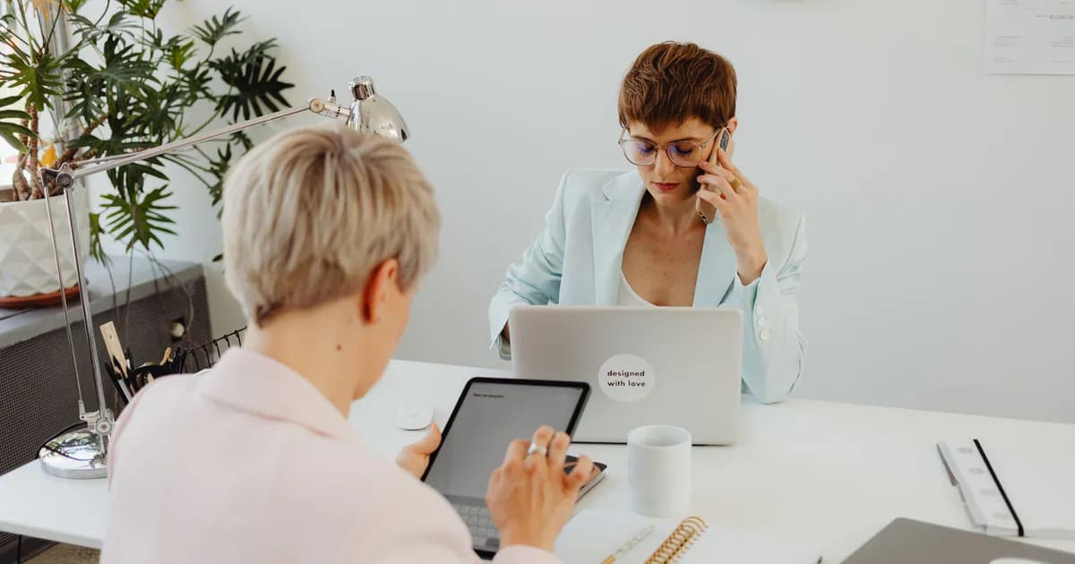Professional women working on laptops and tablets in a modern office setting, focused on teamwork