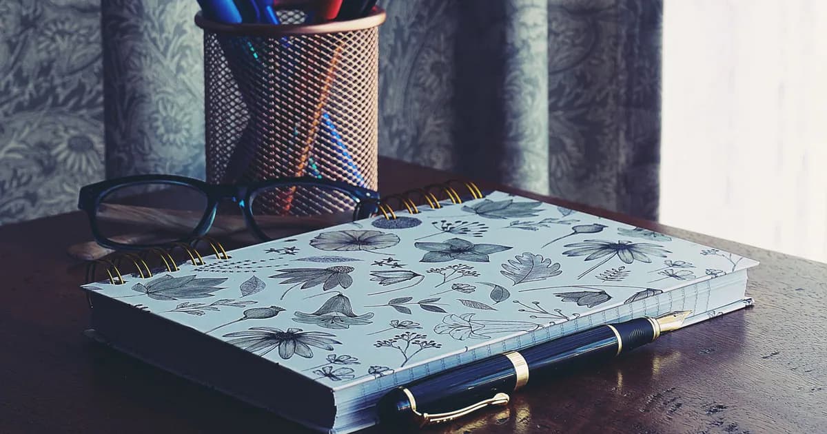 A stylish workspace featuring a floral notebook, glasses, and pens on a wooden desk