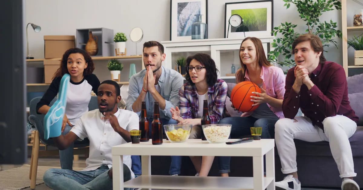 A group of young friends enthusiastically watching a sports event indoors with snacks and drinks