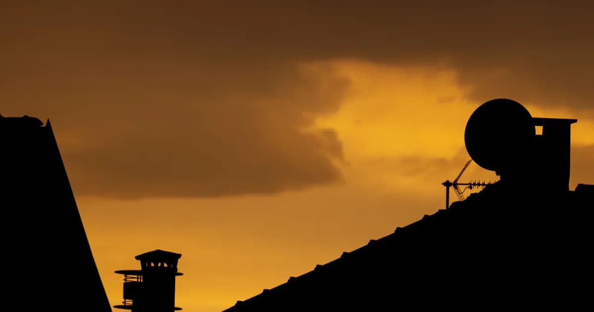 Dramatic silhouette of rooftops and antennas against a vivid sunset sky