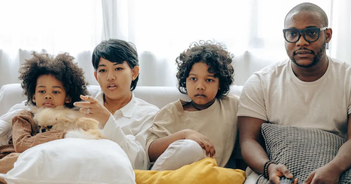 Concentrated multiethnic family watching interesting movie on TV sitting together on cozy couch