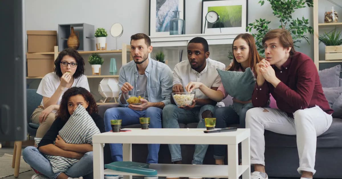Group of friends watching a movie on a couch, enjoying snacks and drinks indoors