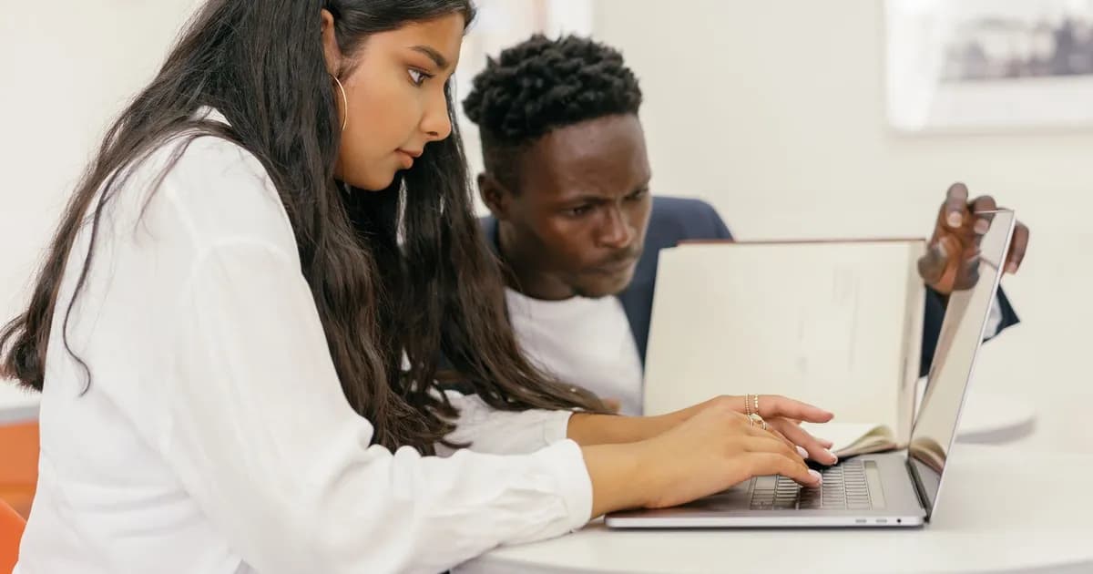 Young woman typing on a laptop while a young man beside her watches the screen