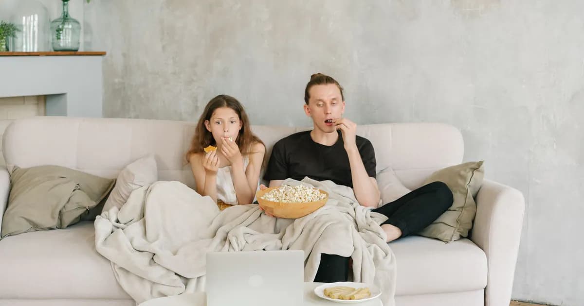 Father and daughter enjoying a cozy movie night with popcorn and snacks on a living room couch