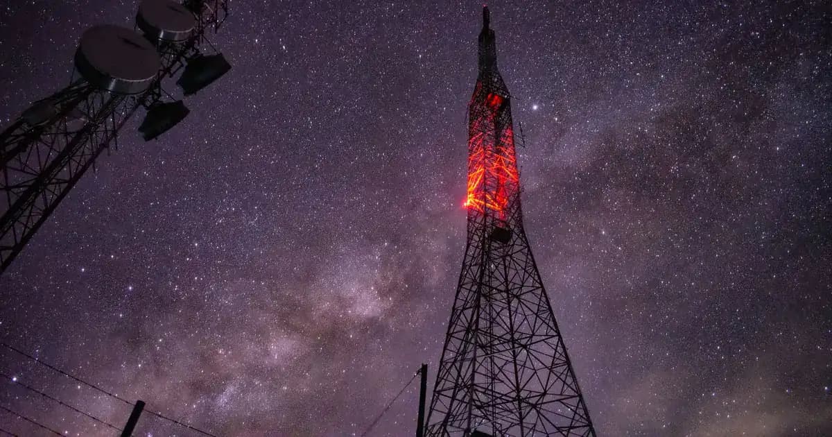 Red-lit lattice radio tower beneath a starry night sky with the Milky Way