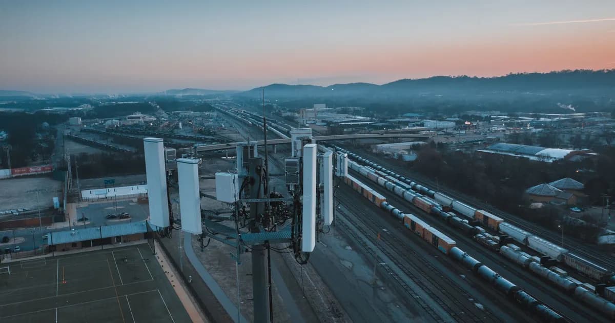 Dusk aerial view of cell tower antennas above a rail yard with distant hills