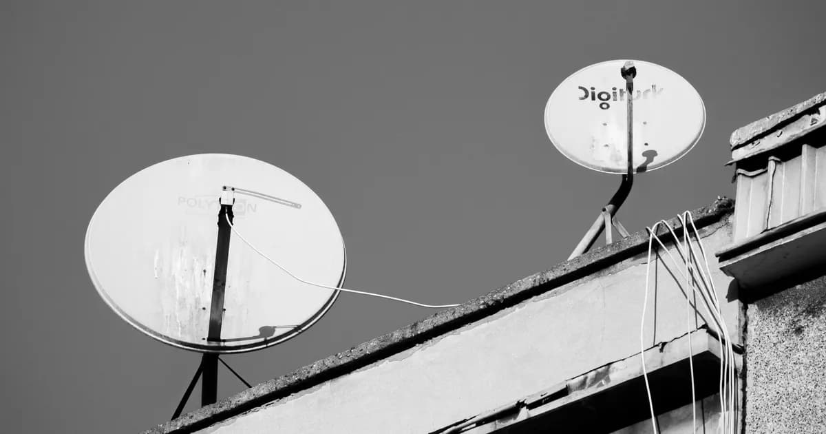 Two satellite dishes mounted on a building rooftop, photographed in black and white