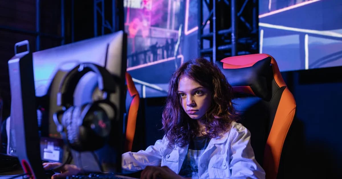 Gamer with long wavy hair seated at a computer in a neon-lit setup