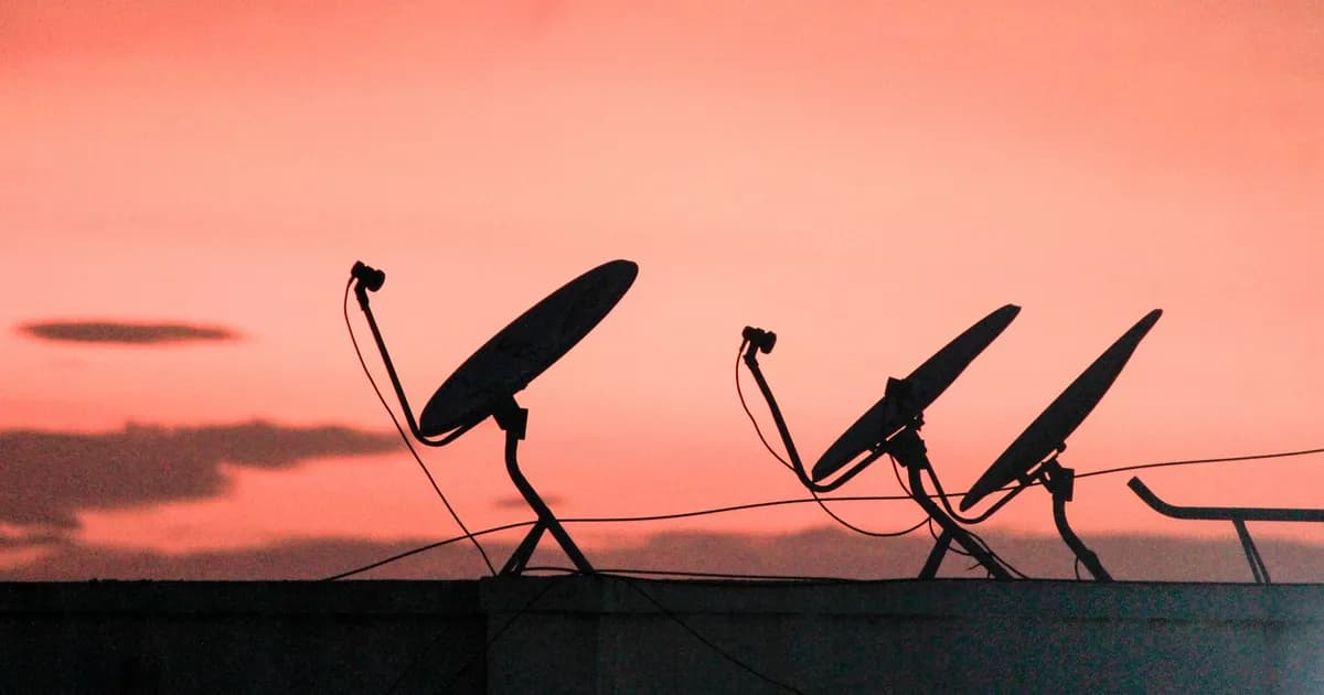 Three satellite dishes silhouetted against a pink and orange sunset sky
