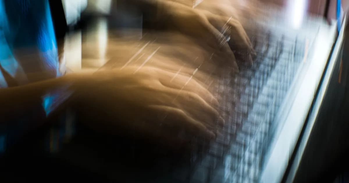 Blurred motion of hands typing quickly on a laptop keyboard in dim light