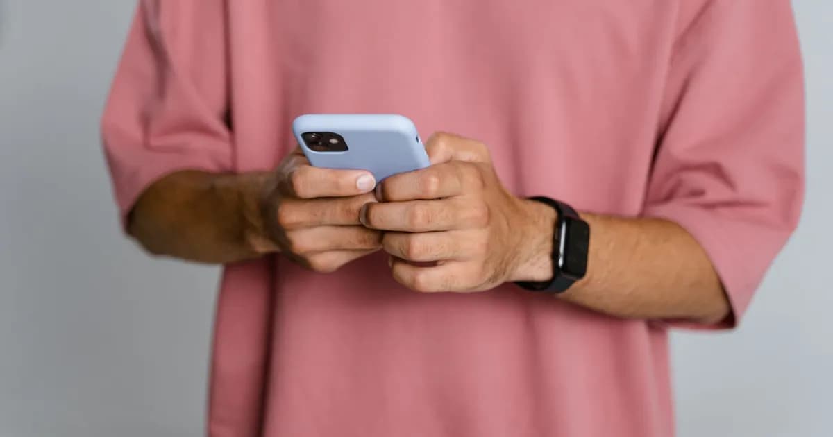Person in a pink t-shirt holding a smartphone, wearing a black smartwatch