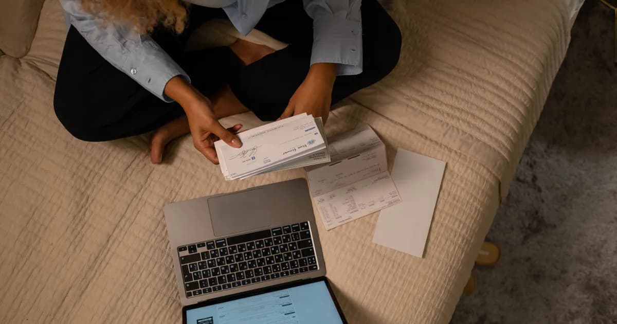 Overhead view of woman organizing finances on bed with laptop and checks
