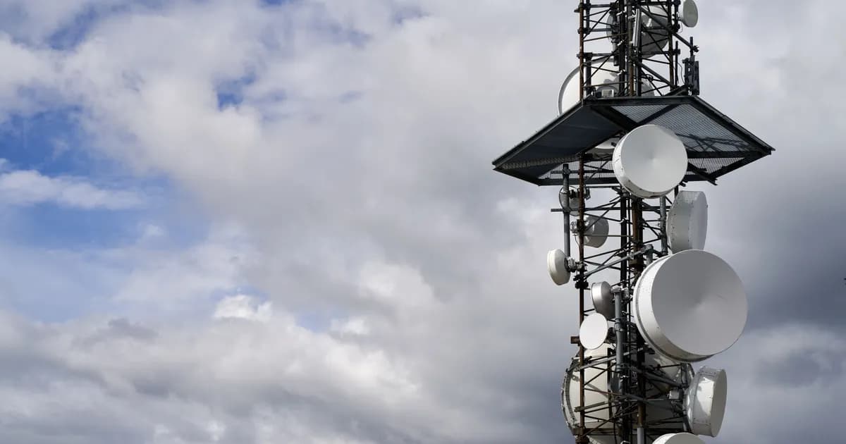 Cell tower with several antennas and dishes against a cloudy blue sky