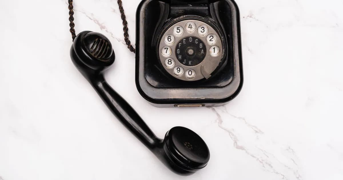 Old-fashioned rotary dial telephone with receiver on white marble background