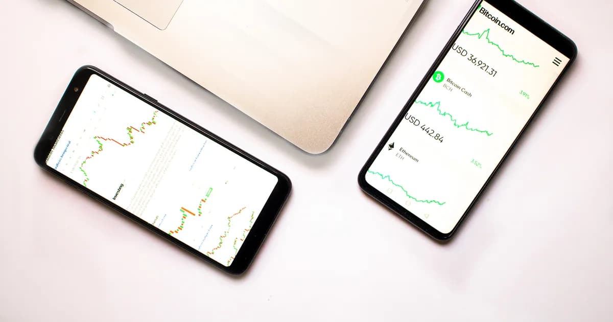 Two smartphones showing line charts beside part of a laptop on a white surface
