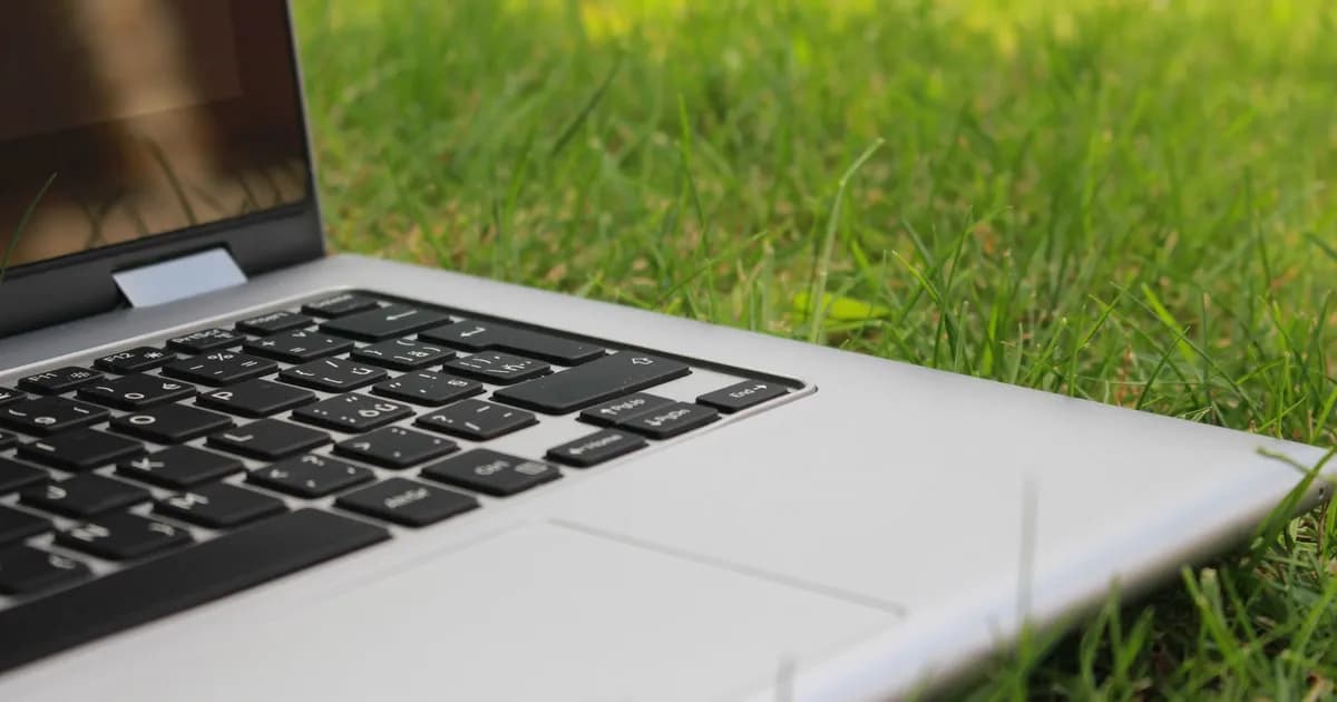 Silver laptop keyboard resting on green grass outdoors