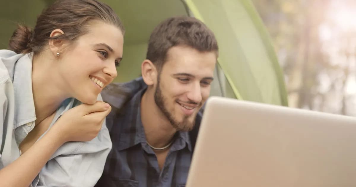 Smiling young man and woman looking together at a laptop outdoors