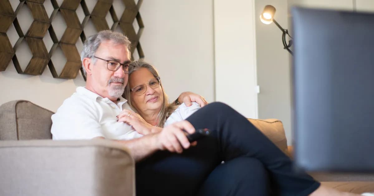 A senior couple enjoys a quiet and happy moment watching television together on the sofa