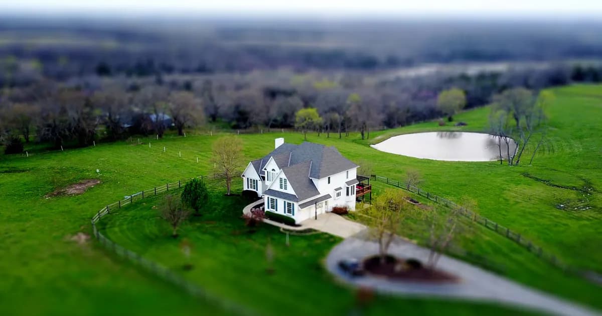 Aerial shot of a charming rural home surrounded by lush green fields and a tranquil pond