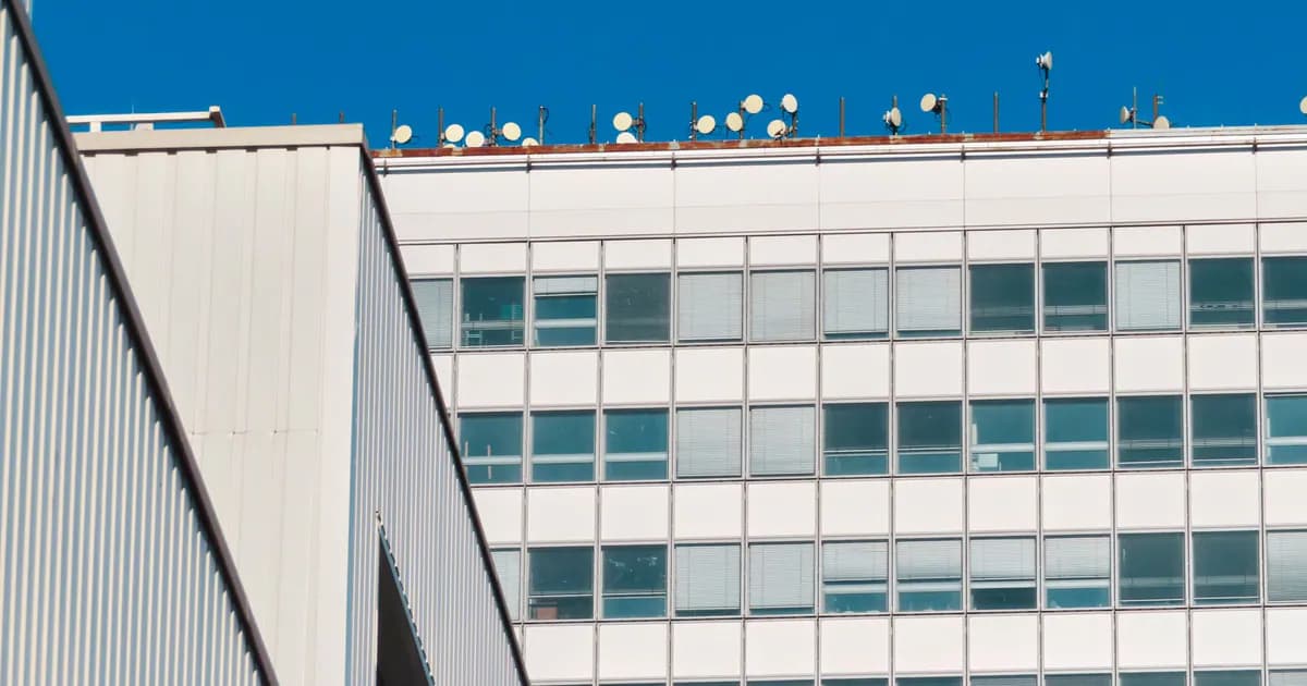Low angle view of a modern building with satellite dishes against a blue sky
