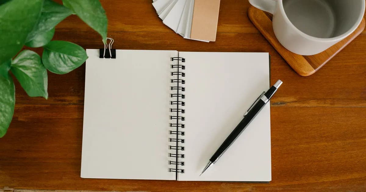 From above empty notebook with pen and tags placed near potted plant and empty mug on office table