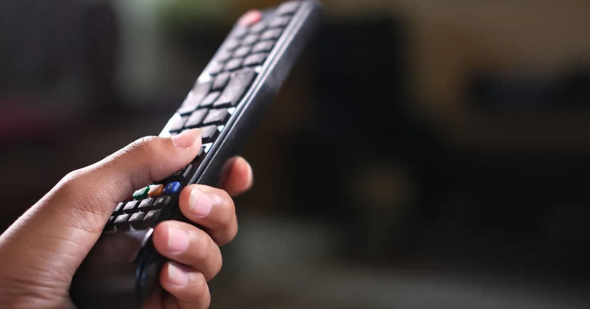 Hand holding a TV remote control, focusing on buttons and grip indoors