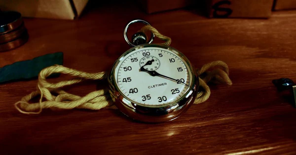 Close-up of an antique silver stopwatch resting on a wooden table with a yellow rope