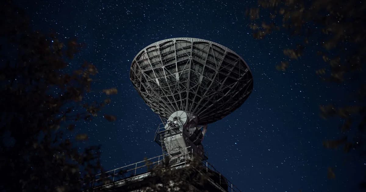 From below of blue starry sky over radio telescope and trees with leaves